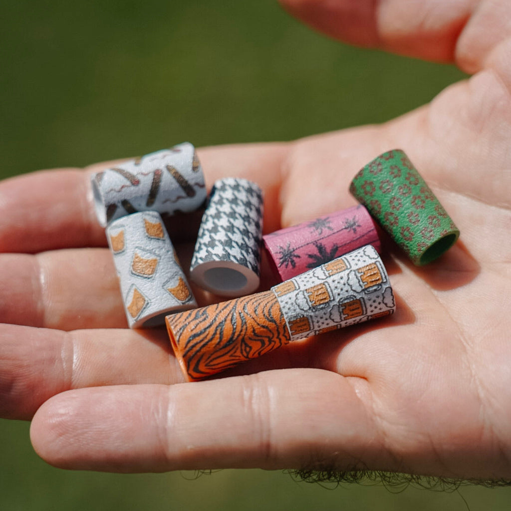 Hand holding colorful patterned ferrules against a blurred green background