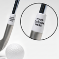A silver golf club head with a white ferrule label reading 'YOUR DESIGN HERE' beside a white golf ball and tees, on a clean white background. A circular inset shows a close-up of the customizable ferrule area.