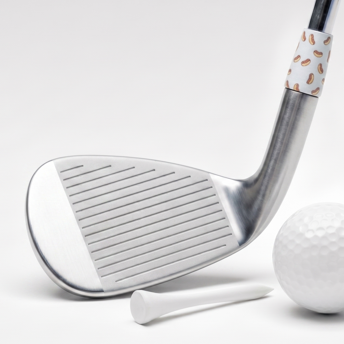 A golf club head with a white ferrule featuring a hot dog pattern, shown alongside a white golf ball, tee, and circular close-up inset of the ferrule detail on a clean white background.