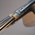 Close-up of a golf club head and shafts featuring a decorative wave-patterned ferrules in blue, beige, and gold tones, with a blurred neutral background.