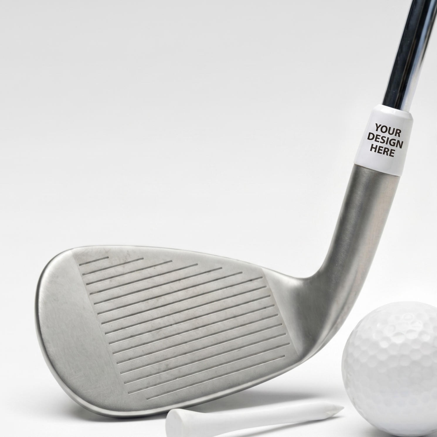 A silver golf club shown on a white background with a white golf ball, tees, and a circular inset highlighting a customizable white ferrule area with the text 'YOUR DESIGN HERE'.